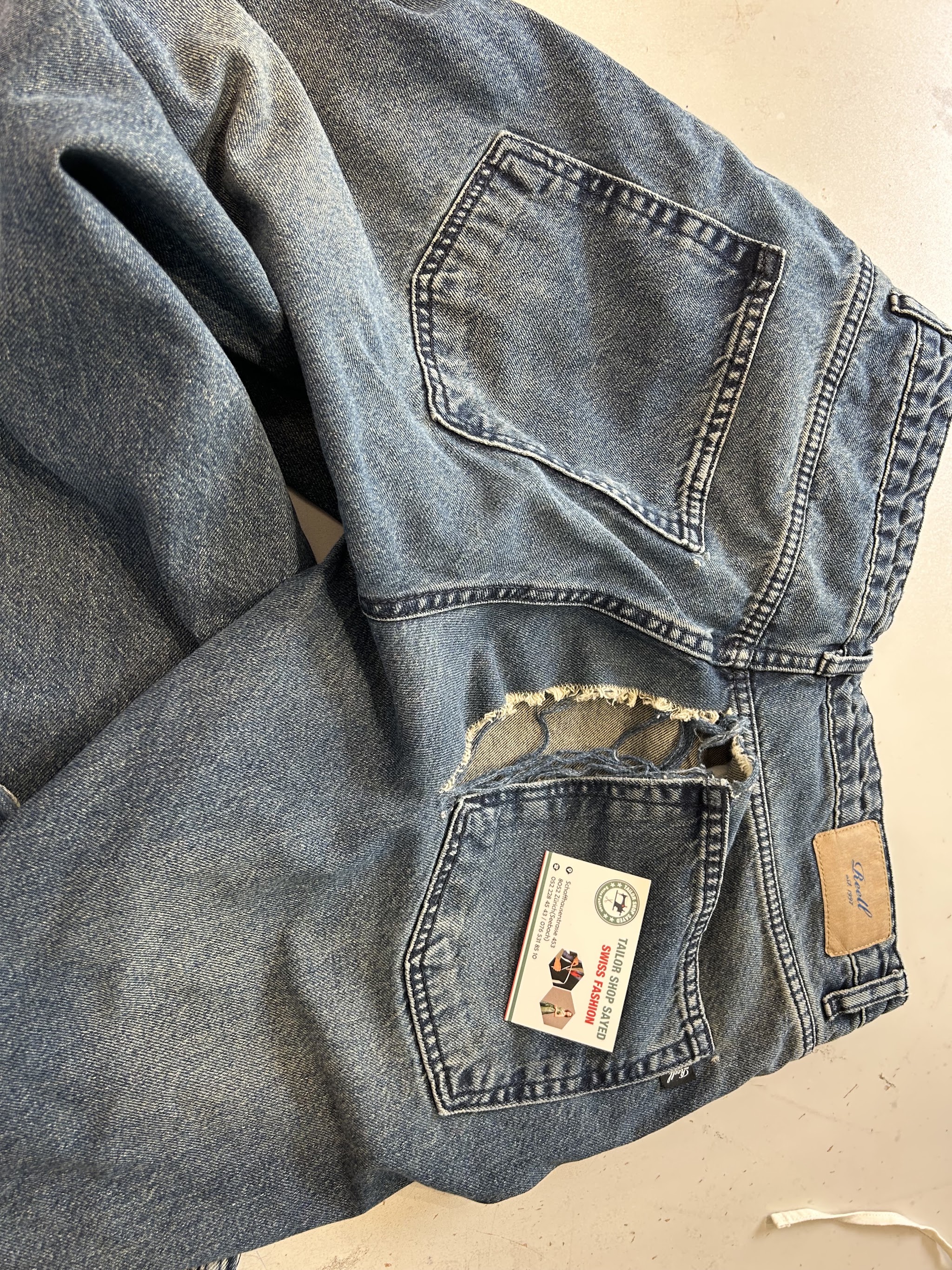 Jeans mit aufgerissener hinterer Tasche auf dem Arbeitstisch, vor der Reparatur